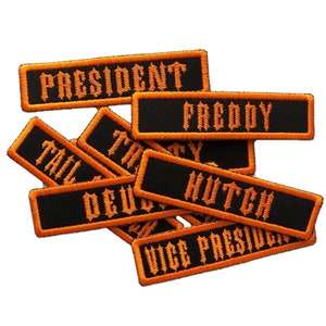 May include: A pile of black and orange embroidered patches with names like "President", "Freddy", "Hutch", and "Vice President".