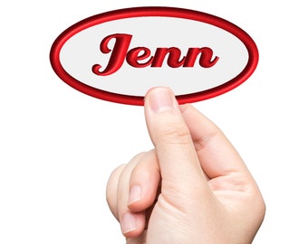 Puede incluir: Una mano sostiene una pegatina ovalada blanca con un borde rojo. La pegatina dice "Jenn" en letras rojas y cursivas.