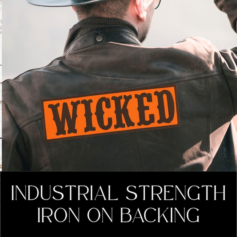 Puede incluir: Una chaqueta de cuero marr&oacute;n con un parche naranja que dice "WICKED" en letras negritas y estilizadas. La imagen tambi&eacute;n incluye el texto "INDUSTRIAL STRENGTH IRON ON BACKING".