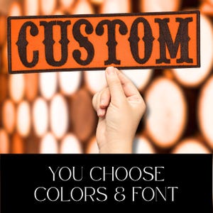Puede incluir: Un parche rectangular naranja con la palabra "CUSTOM" en letras ornamentadas de color marr&oacute;n oscuro. El parche est&aacute; sostenido por una mano. Debajo, el texto dice "YOU CHOOSE COLORS & FONT".