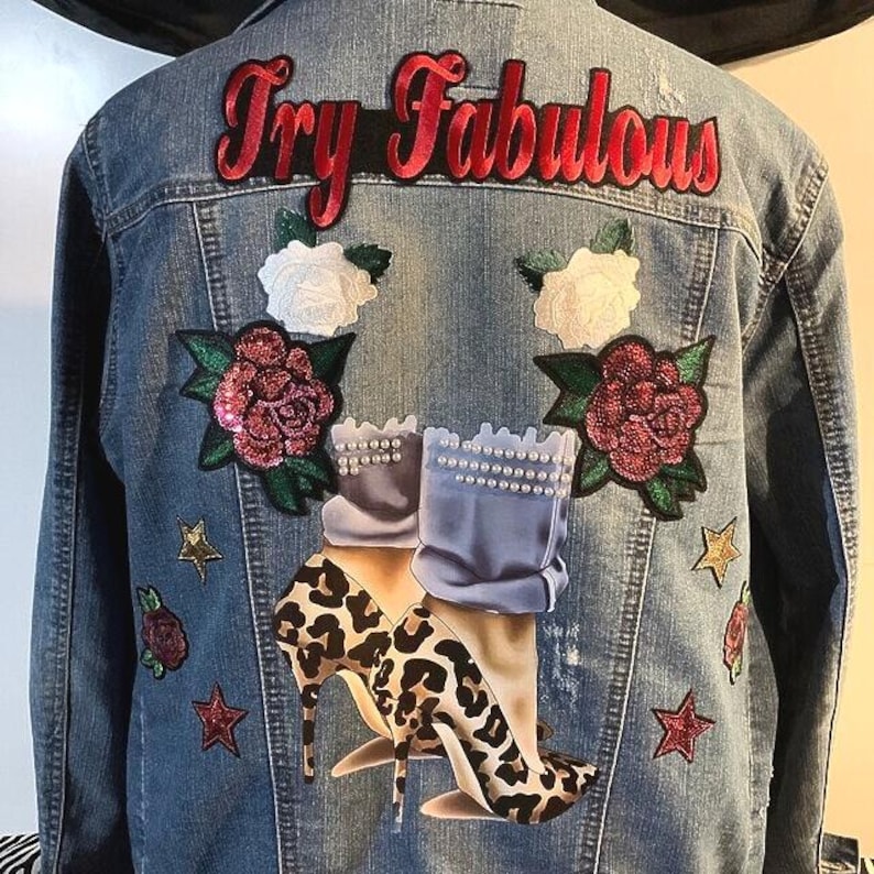 Puede incluir: Una chaqueta de mezclilla azul con el texto Try Fabulous bordado en rojo en la parte superior. La espalda est&aacute; decorada con parches de rosas blancas y rojas, estrellas doradas y rojas, y un gr&aacute;fico de piernas con tacones de leopardo.