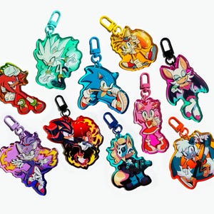 Puede incluir: Colección de llaveros acrílicos coloridos con varios personajes de la franquicia Sonic the Hedgehog. Cada llavero tiene un diseño y esquema de color únicos, con un cierre metálico. Los llaveros se muestran sobre un fondo blanco.