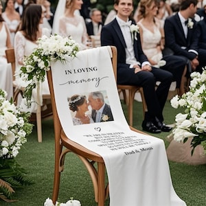 May include: A white fabric chair sash with the words "IN LOVING memory" printed in black script. A photo of a couple is below the text, with additional text and a heart symbol. The sash is draped over a wooden chair.