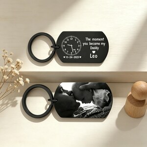 May include: Two black keychains. One features a clock design with the text "The moment you became my Daddy" and the name "Leo." The other keychain displays a black and white photo of a parent and child.
