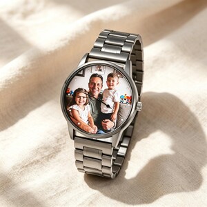 May include: A silver-toned metal wristwatch featuring a custom circular watch face that displays a color photograph of an adult and two children. The timepiece has a linked metal band, a round case, and thin black hands for indicating the time.