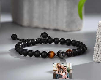 Puede incluir: Pulsera de cuentas negras con cuentas de ojo de tigre y marrón oscuro. La pulsera tiene un acento metálico y una pequeña foto familiar. El texto "Your Photo" está debajo.