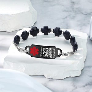 May include: A medical ID bracelet featuring dark blue cross-shaped beads and a black plate with a red medical symbol and a QR code. The text "HEALTH INFO" and "SCAN ME" are also visible.