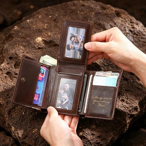Può includere: Un portafoglio in pelle marrone scuro a tre ante con due finestre trasparenti contenenti fotografie, scomparti per carte, uno scomparto per banconote e un'incisione color oro con la scritta I love you more forever and always Elaine.