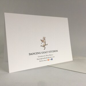 May include: White card with a logo of a goat dancing with a book. The text reads "Dancing Goat Studios" with the tagline "Creations by Mara Bianca" and the website "DancingGoatStudios@yahoo.com". The text "Find my shop on" is followed by icons for Etsy and Facebook.