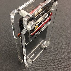 May include: A clear acrylic case with a black circuit board inside. The case has two AA batteries inside and clear plastic standoffs.