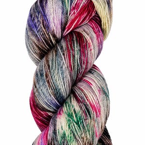 Pode incluir: Uma meada de fio tingido à mão com uma paleta de cores variadas de magenta vibrante, roxo profundo, verde floresta e amarelo dourado, misturadas com estrias de carvão escuro e creme ao longo dos fios de fibra torcidos.