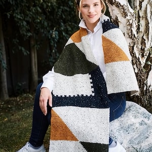 Puede incluir: Una bufanda de punto rectangular con un patrón geométrico de bloques de color en amarillo mostaza, verde oliva oscuro, azul marino y crema moteado. La bufanda está confeccionada con un punto texturizado y muestra segmentos triangulares y rectangulares.