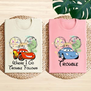 two t-shirts with cartoon car designs and text, placed on a woven mat.