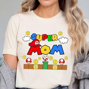 A woman wearing a white t-shirt with a colorful graphic design featuring a character from the Super Mario video game franchise.