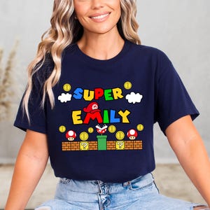 A woman wearing a navy blue t-shirt with a colorful graphic design featuring Mario and the text "SUPER EMILY".