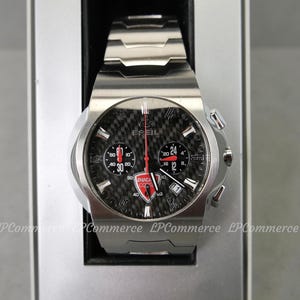 Op de afbeelding: Een roestvrijstalen Breil horloge met een zwarte carbon fiber wijzerplaat. Het horloge heeft rode en witte accenten, een Ducati Corse logo en meerdere sub-wijzerplaten. Het horloge wordt gepresenteerd in een zilveren doos.