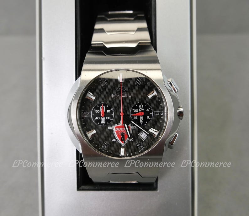 Op de afbeelding: Een roestvrijstalen Breil horloge met een zwarte carbon fiber wijzerplaat. Het horloge heeft rode en witte accenten, een Ducati Corse logo en meerdere sub-wijzerplaten. Het horloge wordt gepresenteerd in een zilveren doos.