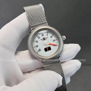 May include: A silver-tone wristwatch with a white circular dial featuring black numerical markers from 5 to 60, a Mini logo, a bright orange hand, and a small digital display showing the number 2. The watch has a metallic mesh strap.