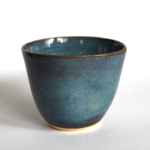 Könnte beinhalten: Eine kleine, tiefblaue Keramikschüssel mit einem dunkelbraunen Rand. Die Schüssel hat eine gesprenkelte, unebene Glasur.