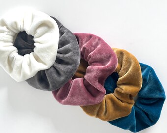 Può includere: Cinque scrunchies di diversi colori. Uno è bianco, uno è grigio, uno è rosa, uno è giallo senape e uno è blu verde.
