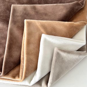 May include: A selection of soft, plush blankets in a range of neutral tones, including browns, tans, white, and grey. The blankets are folded to showcase their textures and colours, creating a cosy and inviting appearance.