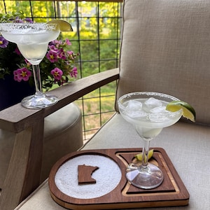 May include: Two margarita cocktails on a wooden coaster with a salt rim and a lime wedge. The coaster features a cutout of the state of Minnesota.
