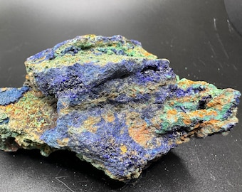 May include: A rough, natural specimen of azurite and malachite. The blue azurite is interspersed with green malachite, creating a striking contrast. The rock has a rough, uneven surface.