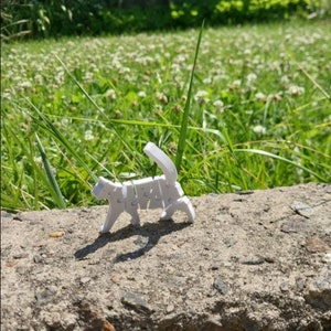 Peut inclure: Un jouet de puzzle en plastique blanc en forme de chat, composé de pièces qui s'emboîtent. Le chat est debout sur une surface en béton gris.