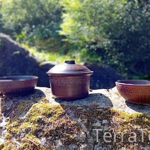 May include: Three brown ceramic bowls with intricate designs are arranged on a mossy rock. The bowls are in a row, with the largest bowl in the centre. The bowls are handmade and have a rustic appearance.