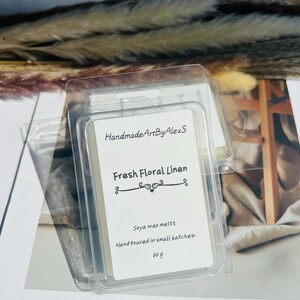 May include: Clear plastic packaging containing soy wax melts. The label reads "Handmade Art By AlexS" and "Fresh Floral Linen." The label also states "Soya wax melts" and "Hand poured in small batches." The package contains 60 g of wax melts.