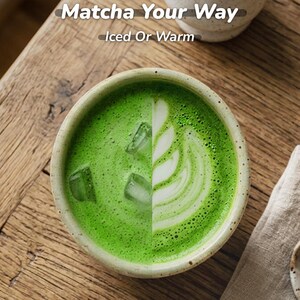May include: A ceramic bowl of matcha tea, split in half to show two preparations. One side is a vibrant green with ice cubes, the other side has a white design. The text "Matcha Your Way" and "Iced Or Warm" is at the top.