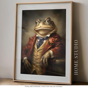 May include: A framed wall art print featuring a portrait of a toad dressed in a brown suit, yellow vest, and blue cravat with a pink rose boutonniere and a ring on its finger. The text HOME STUDIO is printed vertically on the right side of the frame.