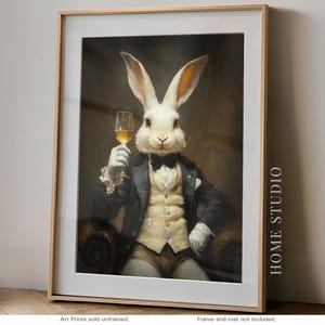 May include: A framed art print featuring a white rabbit dressed in a formal black tuxedo jacket, a cream-colored vest, and a black bow tie. The rabbit holds a glass of golden liquid. The text HOME STUDIO is printed vertically on the right side.