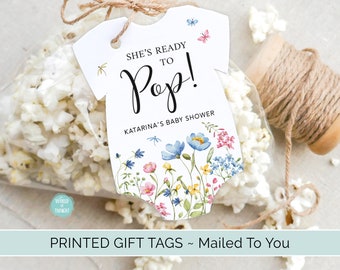 May include: A white baby onesie gift tag with a floral design and the text "She's ready to Pop! Katarina's Baby Shower".