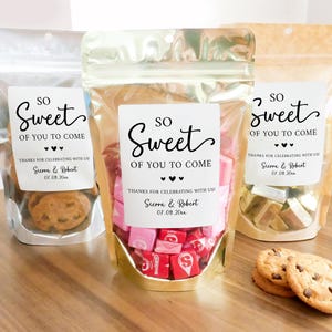 May include: Three clear plastic bags with gold, silver, and brown accents, each filled with different treats. Each bag has a white label with black text that reads "So Sweet Of You To Come" and includes the names Sierra & Robert and the date 07.09.20.