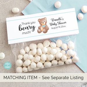 Puede incluir: Una bolsa de regalo blanca con una etiqueta de agradecimiento azul y blanca. La etiqueta presenta un oso marr&oacute;n de dibujos animados con una pajarita azul y el texto "Thank you beary much!" y "Danielle's Baby Shower August 19, 20xx".