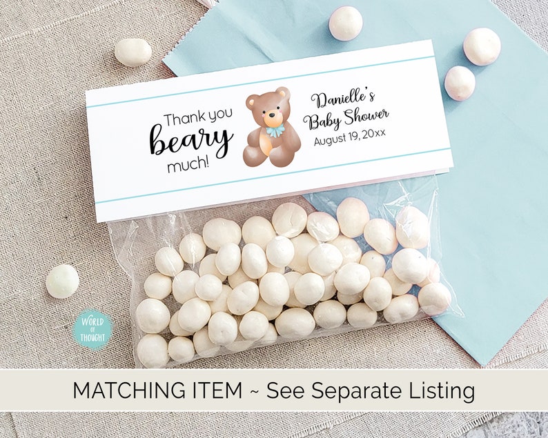 Puede incluir: Una bolsa de regalo blanca con una etiqueta de agradecimiento azul y blanca. La etiqueta presenta un oso marr&oacute;n de dibujos animados con una pajarita azul y el texto "Thank you beary much!" y "Danielle's Baby Shower August 19, 20xx".