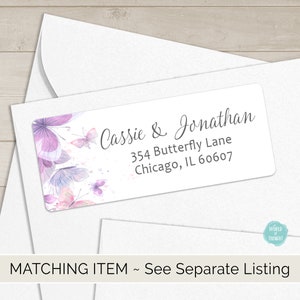 Op de afbeelding: Een witte envelop met een retouradreslabel met een aquarelontwerp van paarse vlinders en de tekst "Cassie & Jonathan, 354 Butterfly Lane, Chicago, IL 60607".