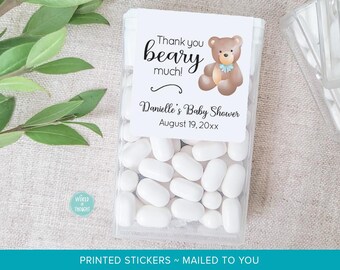 May include: A clear rectangular plastic container filled with white oval candies, featuring a white label with a brown teddy bear illustration, a blue bow, and the text Thank you beary much! Danielle's Baby Shower August 19, 20xx printed in black.