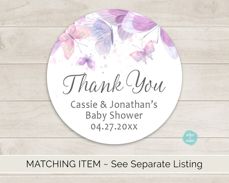 Op de afbeelding: Ronde bedank-sticker met een aquarelontwerp van paarse en roze vlinders op een witte achtergrond. De tekst "Bedankt" staat in een grijs handschrift. Onder de tekst staat "Baby Shower van Cassie & Jonathan 04.27.20XX".