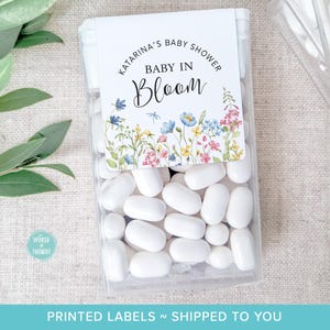 May include: A clear plastic container filled with white mints. A label on the container reads "Katarina's Baby Shower Baby in Bloom" with a floral design.