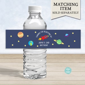 Op de afbeelding: Waterfleslabel met een blauwe achtergrond en sterren. Het label zegt "Bedankt voor het meevieren van Jaime's 2e verjaardag" met een raket, planeten en een UFO.
