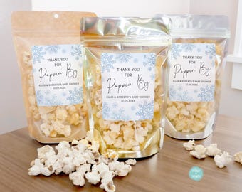 May include: Three clear plastic bags filled with popcorn and tied with a ribbon. Each bag has a white label with blue snowflake designs and the text "Thank you for Poppin' By Allie & Roberto's Baby Shower 12.09.20XX".