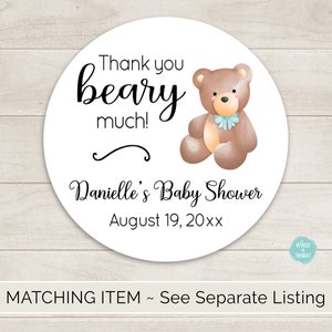 Puede incluir: Pegatina redonda blanca de agradecimiento con texto negro que dice "Thank you beary much!" y "Danielle's Baby Shower August 19, 20xx". Un oso de peluche marr&oacute;n con un lazo azul se encuentra en la esquina superior derecha.