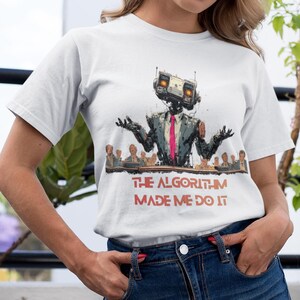 May include: White t-shirt with a graphic of a robot in a suit and tie, with the text "THE ALGORITHM MADE ME DO IT". The robot has a box-shaped head and is standing in front of a group of people. The shirt is paired with a denim skirt.