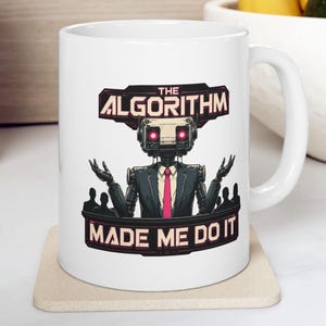 May include: A white ceramic mug featuring a graphic illustration of a robot wearing a suit and pink tie with glowing red eyes. The robot has its hands raised in a shrug gesture. The text reads THE ALGORITHM MADE ME DO IT in bold letters.