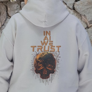 Puede incluir: Sudadera con capucha gris claro con un diseño de calavera y el texto "IN AI WE TRUST" en naranja. La calavera tiene tonos naranja y verde oscuro, con un diseño de placa de circuito.