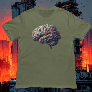 Könnte beinhalten: Olivgrünes T-Shirt mit einer detaillierten Illustration eines Gehirns, das aus Miniaturgebäuden besteht. Das Kunstwerk ist in Braun-, Orange- und Blautönen gehalten. Das T-Shirt hat einen Rundhalsausschnitt und kurze Ärmel, ideal für den Alltag.