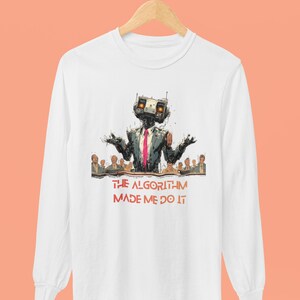 Op de afbeelding: Wit shirt met lange mouwen met een robotillustratie in pak en stropdas, en de rode tekst "THE ALGORITHM MADE ME DO IT". De robot heeft zijn armen open, met een groep mensen op de achtergrond.