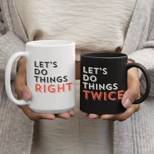 May include: Two ceramic mugs, one white and one black, each with a black handle. The white mug reads "LET'S DO THINGS RIGHT" in black and coral lettering. The black mug reads "LET'S DO THINGS TWICE" in white and coral lettering.
